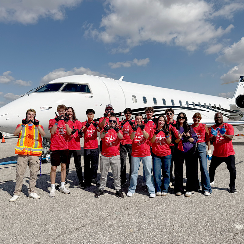 A group of Western commercial aviation management students stand in front of a private jet.